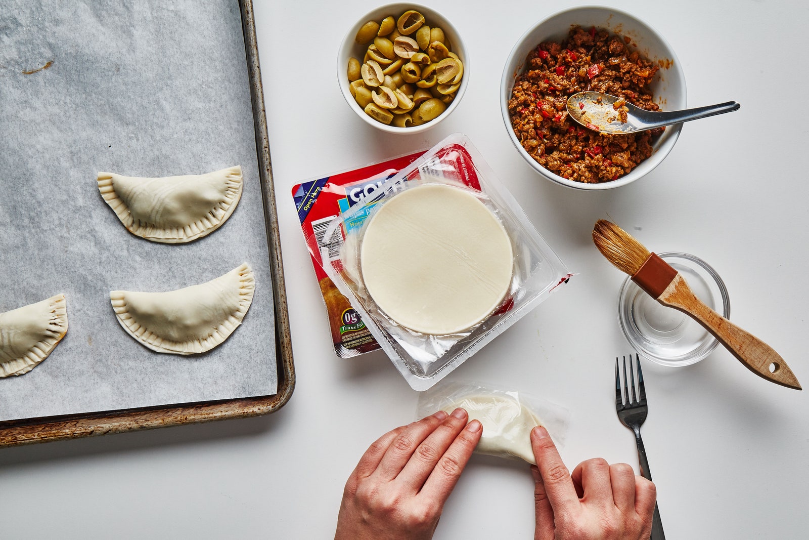 Hands using the plastic wrapper to seal empanada dough around filling.
