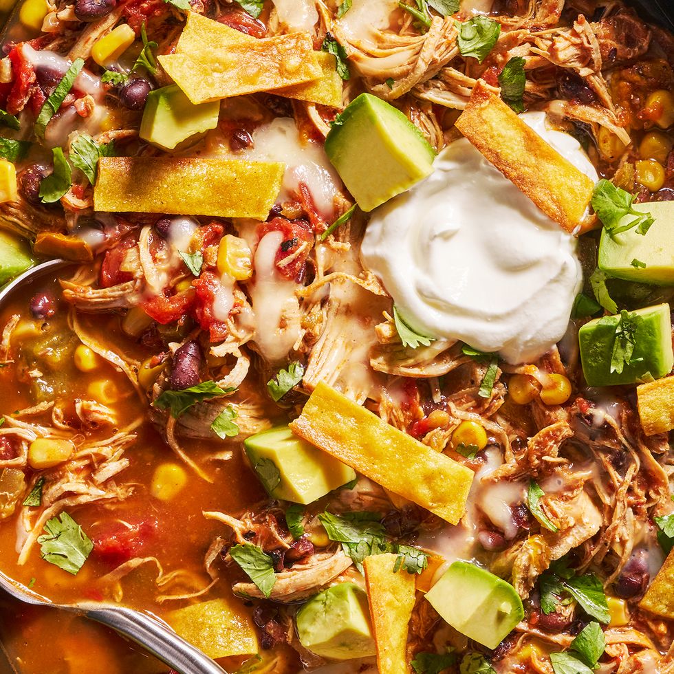 slow cooker chicken tortilla soup with sour cream, avocado slices, cheese and tortilla strips